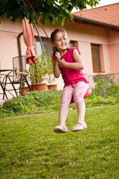 Happy smiling girl swinging on seesaw outdoors (house in the background)