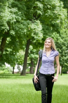 Young business woman wit laptob bag walking outdoors in park