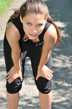 Young person (woman) having break after running in park - bending position