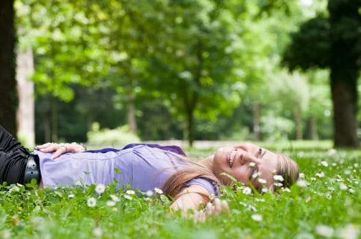 Detail of young woman lying in fresh green grass with flowers - low angle view