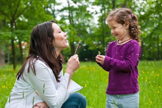 Mother with small daughter blowing to dandelion - lifestyle outdoors scene in park