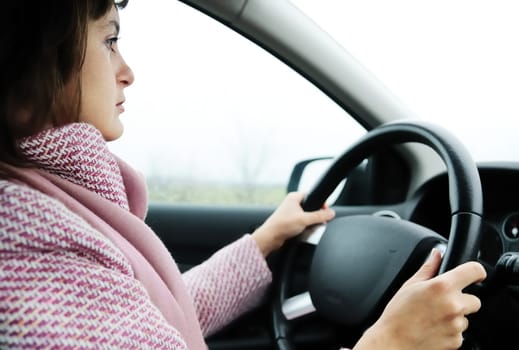 Young business woman driving car in rain (focus on face)