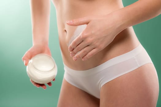 Woman apply body cream on belly slim silhouette on green
