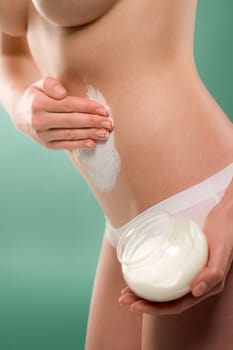 Woman apply body cream on belly slim silhouette on green