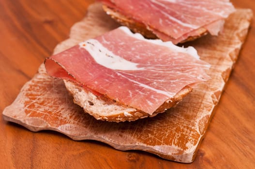 a wooden board with sandwiches topped with raw ham