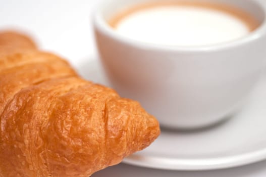 A close-up of a Crossiant and a cup of cappuccino