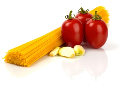 Spaghetti noodles with tomatoes and garlic cloves against a white background