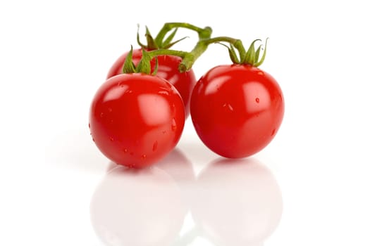 Three fresh cocktail tomatoes mirrored and covered with drops of water