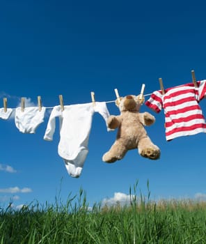Baby Clothing and a teddybear on a clothesline towards blue sky