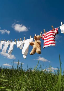 Baby Clothing and a teddybear on a clothesline towards blue sky