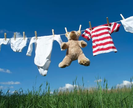 Baby Clothing and a teddybear on a clothesline towards blue sky
