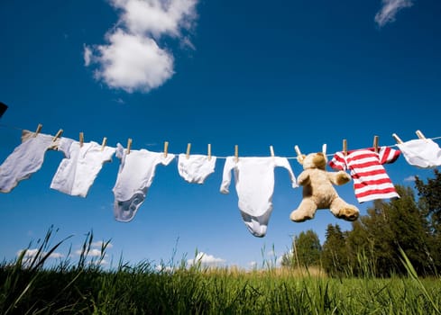 Baby Clothing and a teddybear on a clothesline towards blue sky