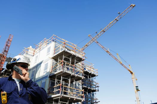 site-worker, talking in phone, cranes and scaffoldings in background
