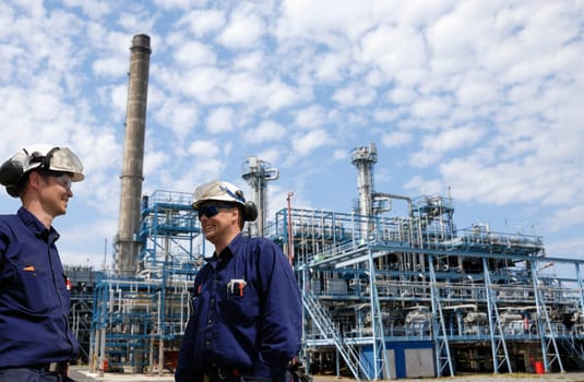 two oil-workers, engineers, with large oil and gas industry in background
