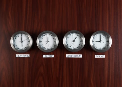 Four clocks with different time on Teak background