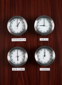 Four clocks with different time on Teak background