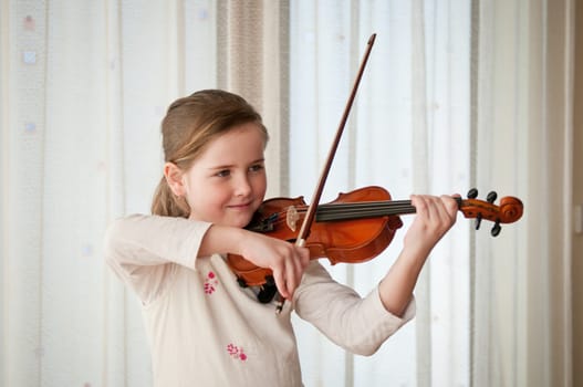 Cute child (little girl) playing violin and exercising at home
