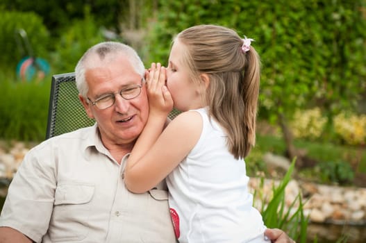 Natural portrait of grandchild whispering to ear of her grandfather in backyard
