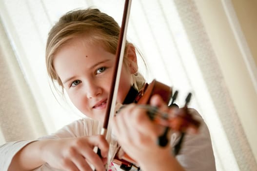 Cute child (little girl) playing violin and exercising at home