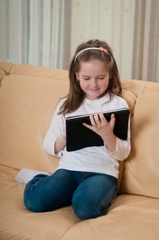 Little child (cute girl) playing with tablet at home sitting on sofa