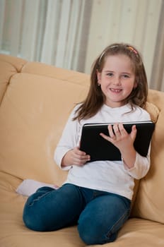 Little child (cute girl) playing with tablet at home sitting on sofa