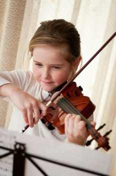Cute child (little girl) playing violin and exercising at home