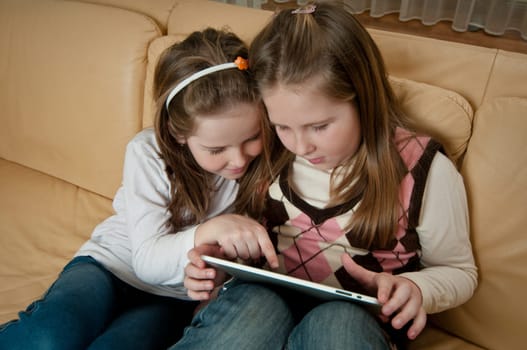 Children (sisters) playing with tablet at home on sofa