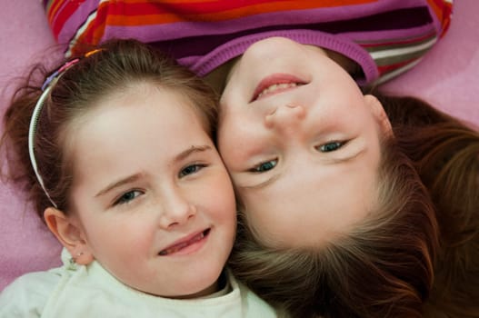 Portrait of smiling cute children (sisters) at home lying in bed
