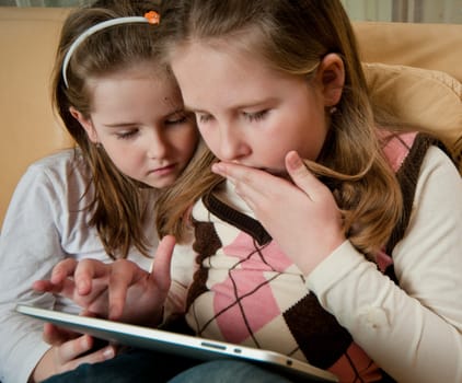 Children (sisters) playing with tablet at home on sofa