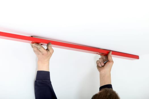 Arms of a man holding a red metal mason&#039 s spirit level to the ceiling during DIY renovations