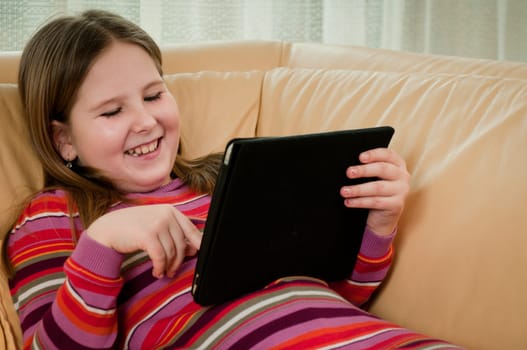 Child (cute girl) playing with tablet at home lying on sofa