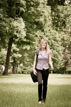 Young business woman wit laptob bag walking outdoors in park