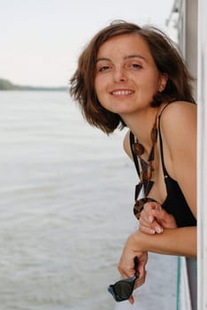 Young smiling woman rests over rail on boat river trip