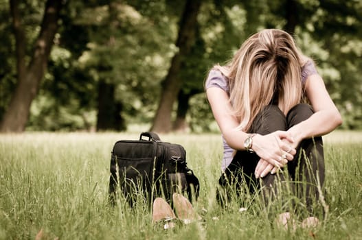 Young depressed business woman siting in grass - notebook bag and shoes lying next