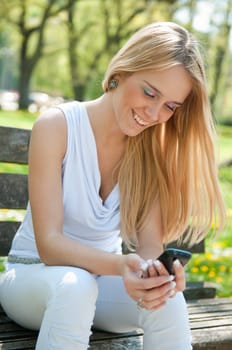 Smiling teen person with mobile phone sitting outdoors on bench