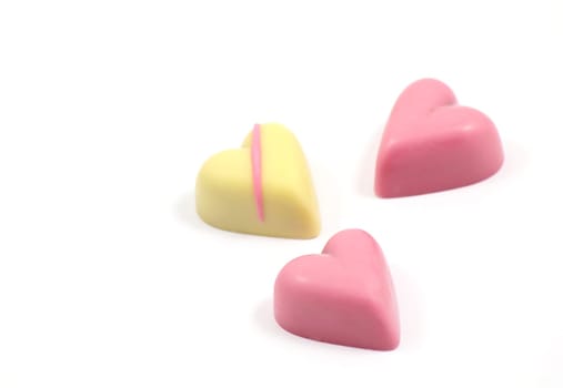 3 heart shaped chocolates, pink and cream, on a white background