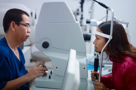 Asian doctor at work during eyesight exam to adult woman in hospital. Side view