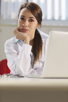 Portrait of mid adult attractive woman smiling at work as doctor with pc in hospital office. Copy space