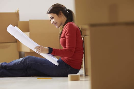 mid adult happy woman moving with boxes at new home and looking at blueprint. Side view, Copy space
