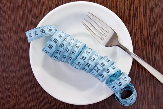 concept for healthy eating. plate with measuring tape and fork