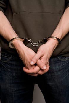 Unreconizable teenager with handcuffs on grey background