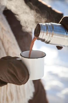 Pouring hot chocolate from a thermos to a mug on a winter day outdoors