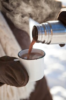 Pouring hot chocolate from a thermos to a mug on a winter day outdoors