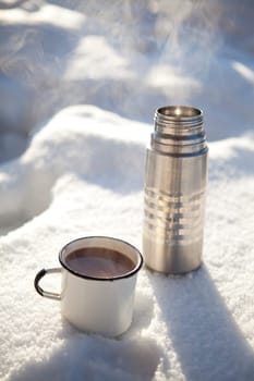 Mug and thermos of hot chocolate on a cold winter day in snow