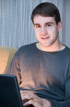 Upper body shot of young man in gray sweatshirt with laptop looking at camera