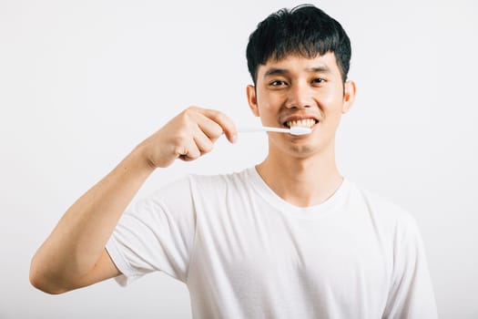 Smiling Asian young man demonstrates proper toothbrushing for dental health. Studio shot isolated on white background, promoting oral care and dentistry.