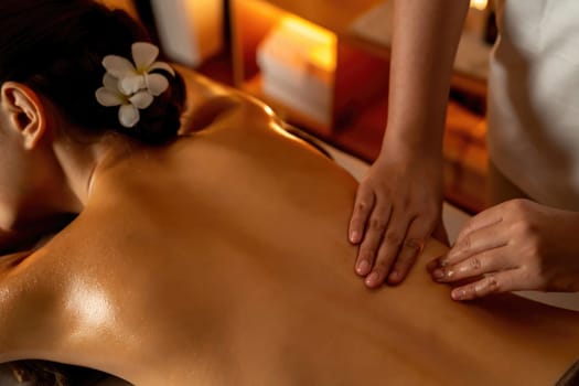 Closeup woman customer enjoying relaxing anti-stress spa massage and pampering with beauty skin recreation leisure in warm candle lighting ambient salon spa at luxury resort or hotel. Quiescent