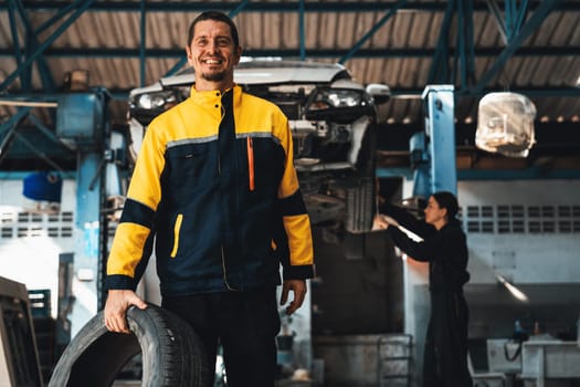 Confident and happy mechanic portrait with smile and wearing uniform standing on automotive service workshop with car lifted on vehicle inspection station background. Oxus