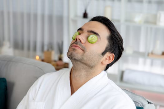 Serene daylight ambiance of spa salon, man customer indulges in rejuvenating with luxurious cucumber facial care. Facial skincare treatment and beauty care concept. Quiescent