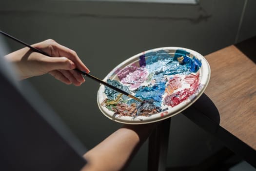 artist brush mix color painting on palette is holding in his hand closeup.